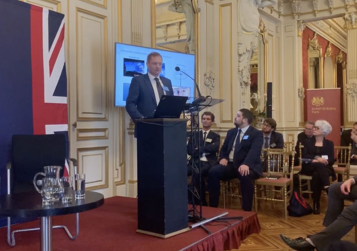 Adam speaking at a lectern at the British Embassy in Paris